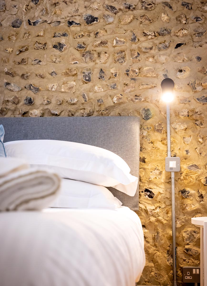 Bedroom against an exposed flint wall with a reading light